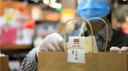 Vendedora com máscara colocando compra em uma sacola de papel